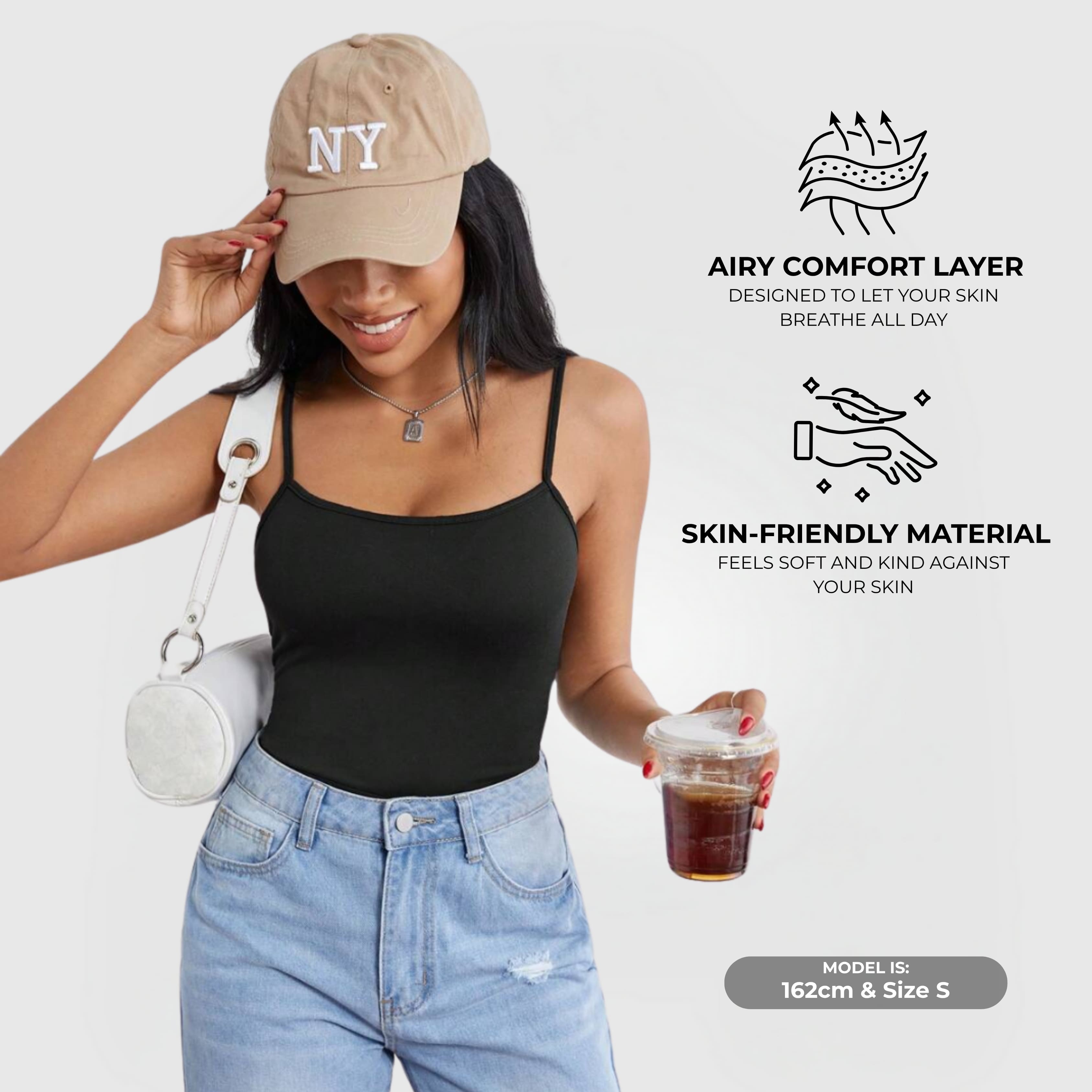 Essential Cami Top – Black worn by a woman paired with jeans and a beige cap in a casual look.